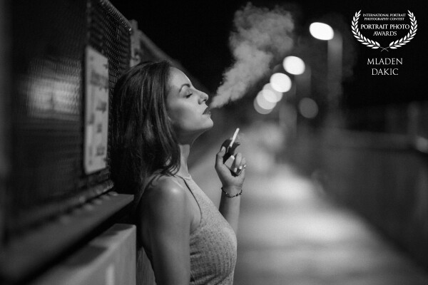 "My last, tonight" means my last cigarette for tonight and shows my beautiful model Mirjam smoking her cigarette with pleasure. A nice detail is, that the smoke is so clearly visible. The light comes from the street lamps only.
