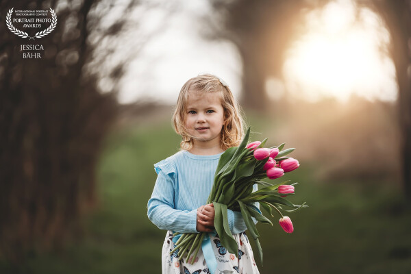 ein kleines blondes Mädchen hält einen Strauß Tulpen in der Hand und schaut in Richtung des Betrachters