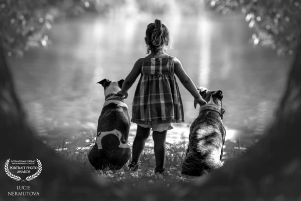 In the silence of black and white, where time briefly stands still, a girl stands with her loyal companions before the endless horizon of the lake. They are connected by a bond unseen but felt by anyone who looks. Together, they face the unknown, gazing into the distance where the worlds of hopes and dreams meet. Three souls intertwined in their own harmony, in a world where words aren't needed, because their hearts speak for them.