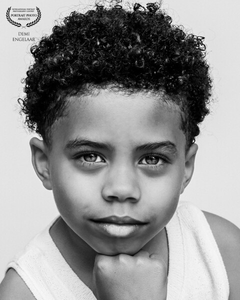 A black and white portrait of a little boy, his face calm and thoughtful. The contrast highlights hi...
