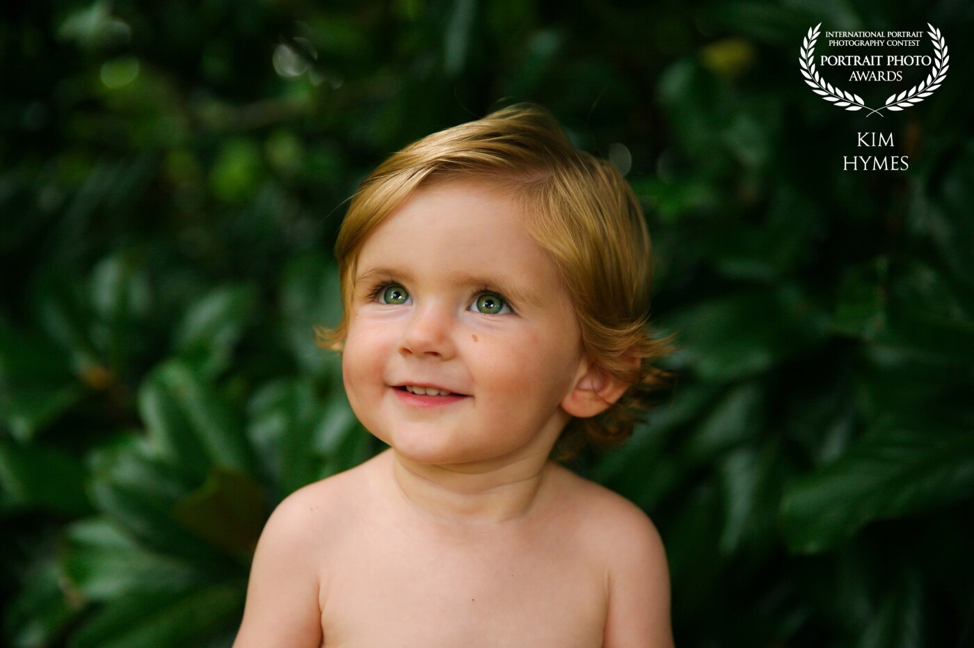 This portrait was taken as it began to rain and we took cover under the magnolia tree. I took off his little shirt because it had a stain. This portrait was taken right before his first haircut. The natural light with his red toned hair and green eyes were just beautiful!  <br />
@kimhymesphotography.com