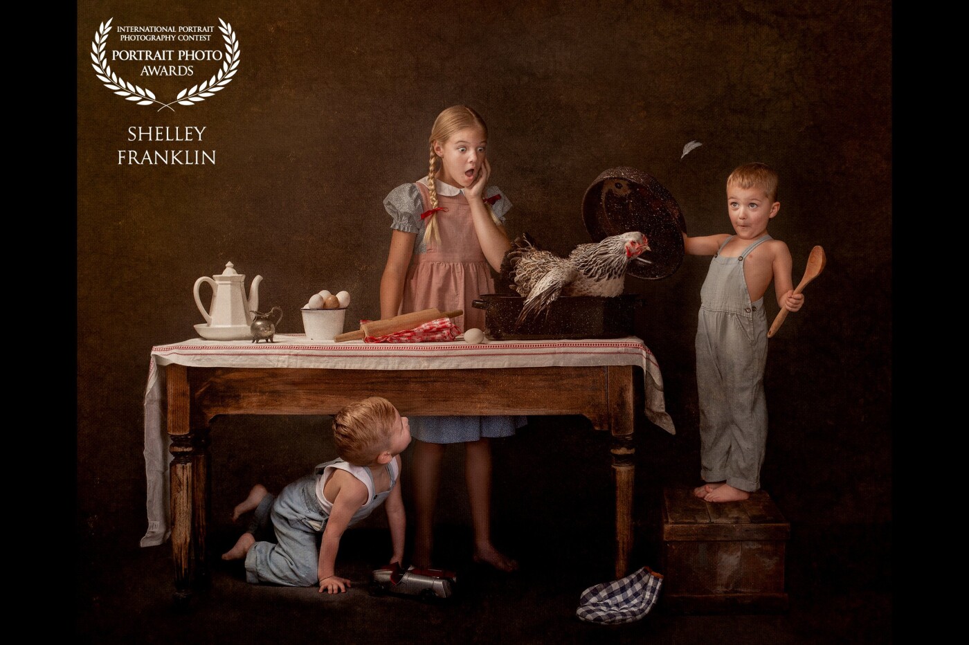 This photo was inspired by stories I heard as a child from my grandparents and my dad about his childhood growing up in a farm in rural Iowa. The working title of the photo was “1951” which was the year my dad was 4 years old. The same age as the little boy standing at the table. <br />
<br />
I’ve always loved looking at the photos of him and his siblings, always running around in overalls and no shoes, summer sun-bleached hair. It seems like there were always animals in the photos with them. Cows, ducks, horses, dogs, and cats must have surrounded these children every day. I don’t recall seeing photos of them with a chicken, but it’s easy to imagine there were chickens there too. <br />
<br />
This is a story of a day in the life of farm children in 1951. While their parents worked in the field all spring they were left alone and unlike kids of today, they were expected to fend for themselves By making breakfast and lunch and complete a list of chores. Of course, it was never all work and no play. These kids could get up to some shenanigans while their parents were hard at work and loved to play tricks on each other. <br />
<br />
The image is a composite and four separate photos were combined to create it. Each child was photographed in their own photo on different days, and all four shoots took place over the span of a month. Editing was a little rough because I had to take the set down between each shoot to use the space for client photoshoots and it was hard to set it up exactly the same and shoot it from the proper angle (I was not using a tripod and did not mark the floor to remind myself where I should take the photo le from) it was all trial and error and I learned so much planning and executing this vision. I can’t wait to create more images this way with what I learned during the process. <br />