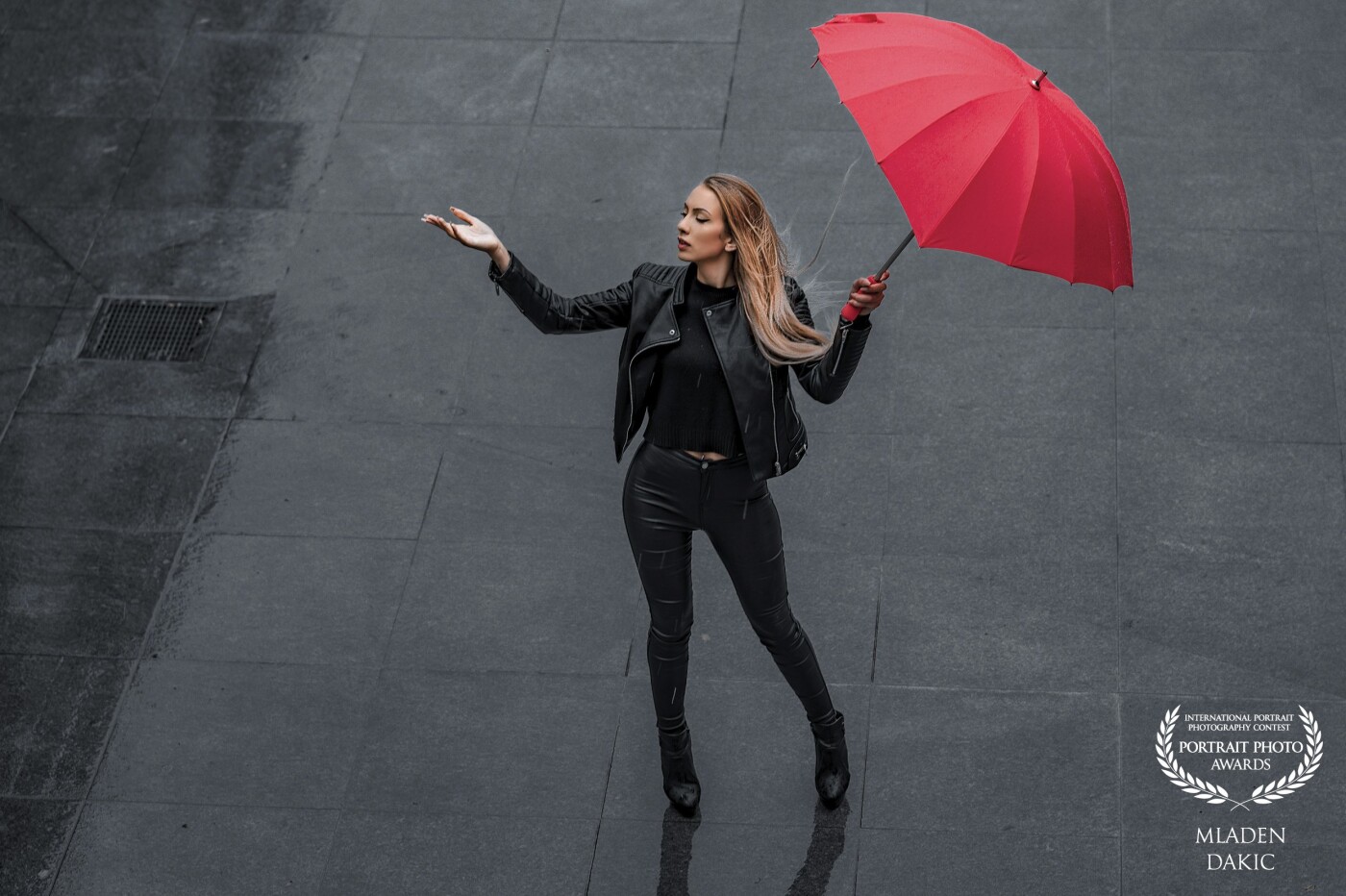 This is a picture from my first photo shoot with Tanja (and it wasn't the last ;-) We had the idea to do some cool city fashion shoots in black leather. The day came and so did the rain. So we took some great shots in the rain.<br />
<br />
I shot her from a higher position. I love the color contrast from the deep black of her leather suit, the gray floor and the red umbrella. I titled the picture "Is it still raining?".<br />
<br />
For this image I only used natural light.