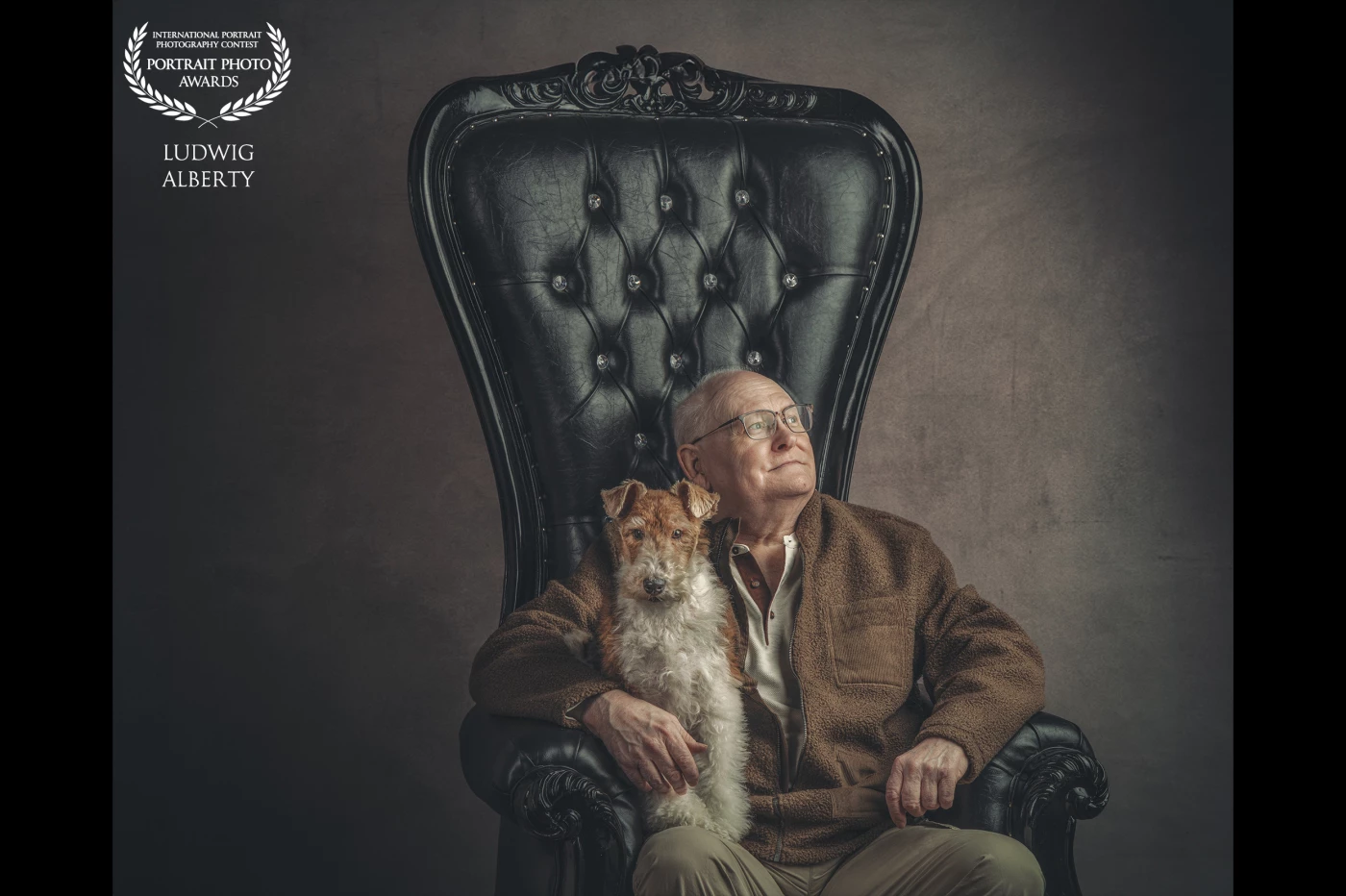 An older man sits confidently on a grand, black tufted chair with ornate detailing. He wears a brown fleece jacket and glasses, exuding wisdom and calm presence. A small terrier dog sits calmly on his lap, both looking off to the side with thoughtful expressions. The background is minimal and dark, drawing all focus to the emotional connection between the man and his pet. The lighting is moody and artistic, reminiscent of classic oil portraiture.