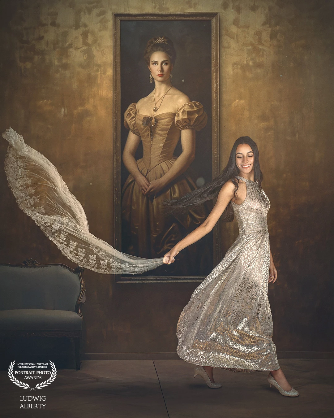 The same woman appears, smiling and twirling slightly, still in her elegant gown. She is playfully holding a piece of sheer lace fabric that flows behind her. The background features a large, stately portrait of a noblewoman in a golden dress, echoing the modern subject’s elegance. The gold-toned setting and matching elements between the portrait and the real figure suggest a connection between past and present — almost like stepping out of the painting.