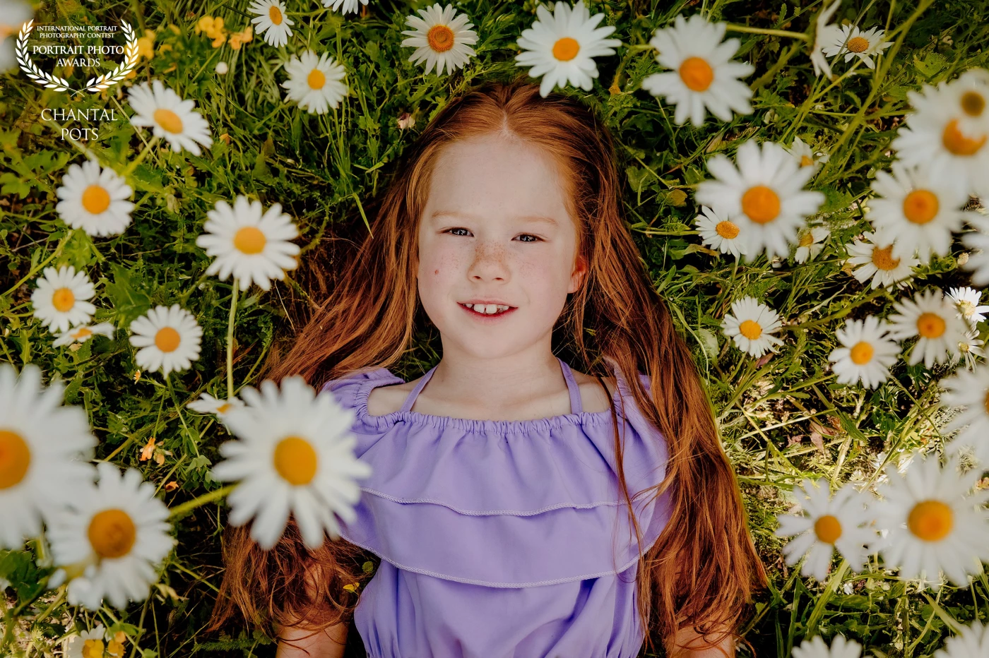 a young girl with flowing red hair lies peacefully among blooming daisies. Her lavender dress and joyful expression radiate innocence and the carefree spirit of childhood, perfectly framed by nature’s gentle beauty.