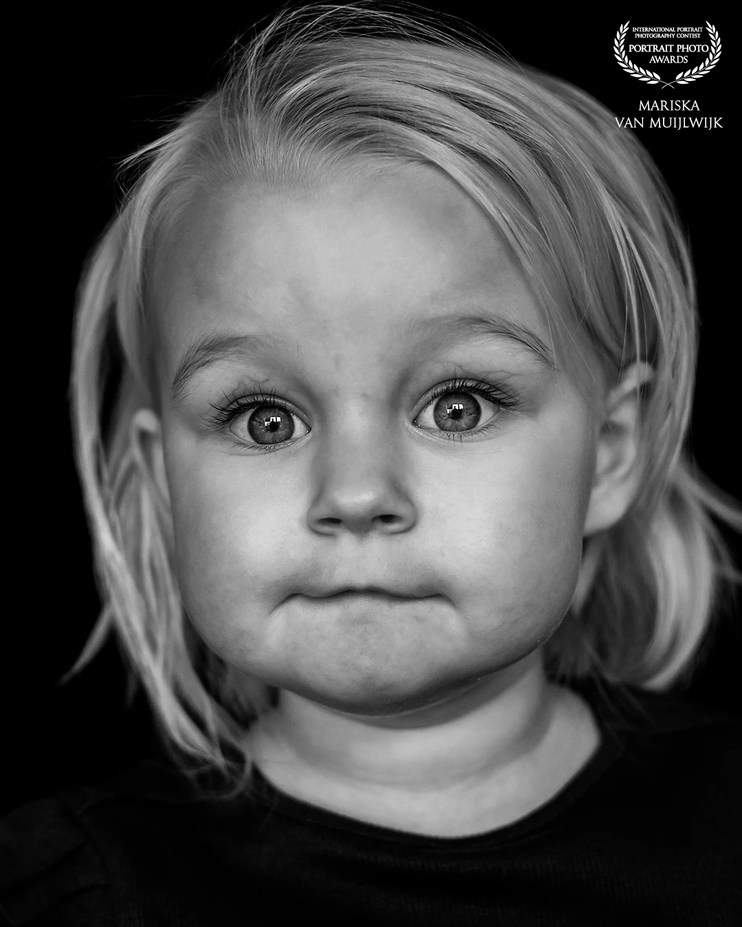 A simple, natural portrait of a young girl. Photographed in black and white, with focus on her direct gaze and facial details. A calm and honest image where minimalism speaks for itself.