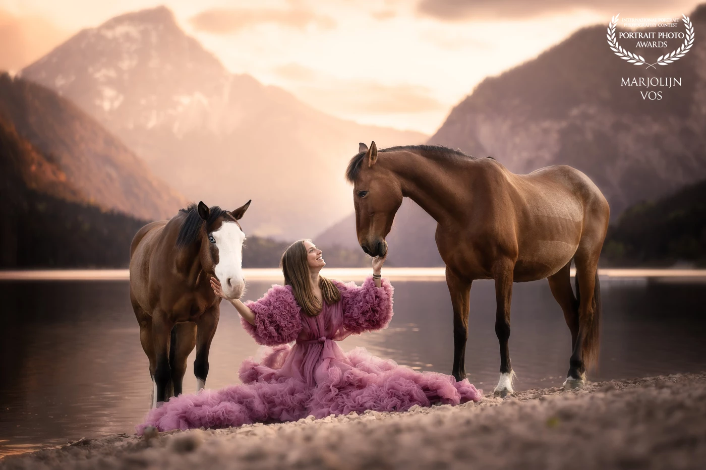 On the quiet shores of Lake Plansee, bathed in the gentle morning light, a moment of pure harmony unfolds. Dressed in a soft rose gown, a magical connection between human and horse. Her two horses bow tenderly towards her, as if answering her heart with a whisper.<br />
A silent story of trust, friendship, and the beauty of simply being together.