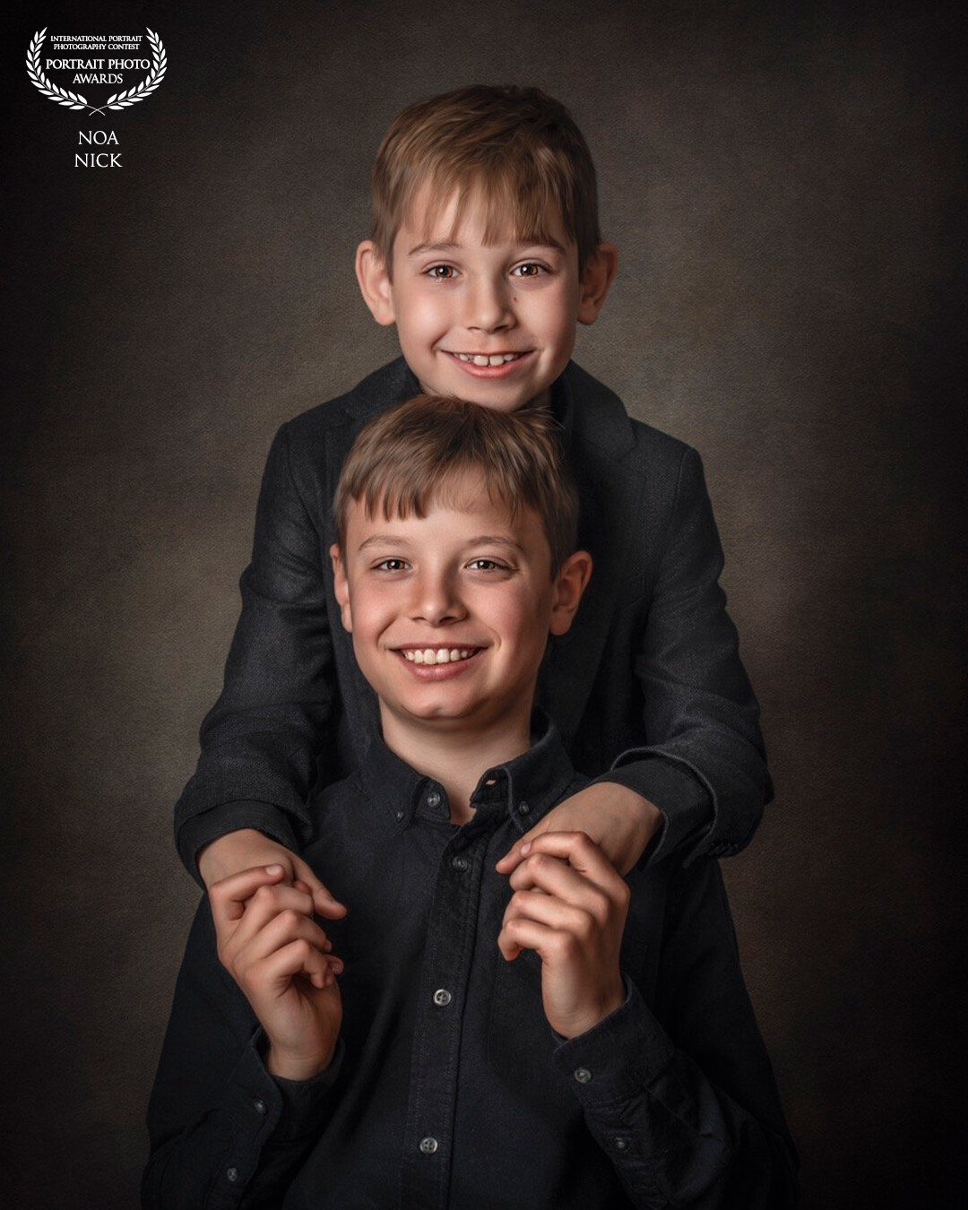 This image captures a heartwarming moment between two boy siblings, with the younger brother lovingly embracing his older sibling from behind. Their faces are lit up with genuine smiles, reflecting a bond that goes beyond mere friendship. The younger boy's arms wrapped around his older brother convey a sense of trust, admiration, and deep connection. The background is intentionally subdued, directing focus to the subjects, and the composition and lighting highlight the innocence and pure joy of the moment. This photograph isn't just a portrayal of two brothers; it's a celebration of family, love, and the unspoken understanding that exists within this special relationship.